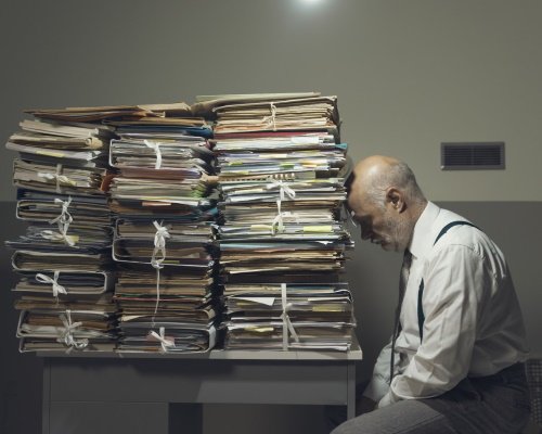 A man is overwhelmed by the quantity of paper documents he has to go through